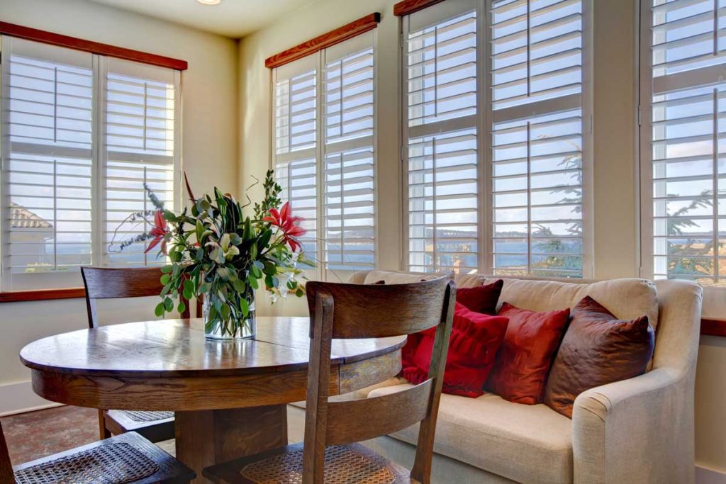 Light tones beautiful dining area with a rustic dining table set, beige sofa and bright red pillows